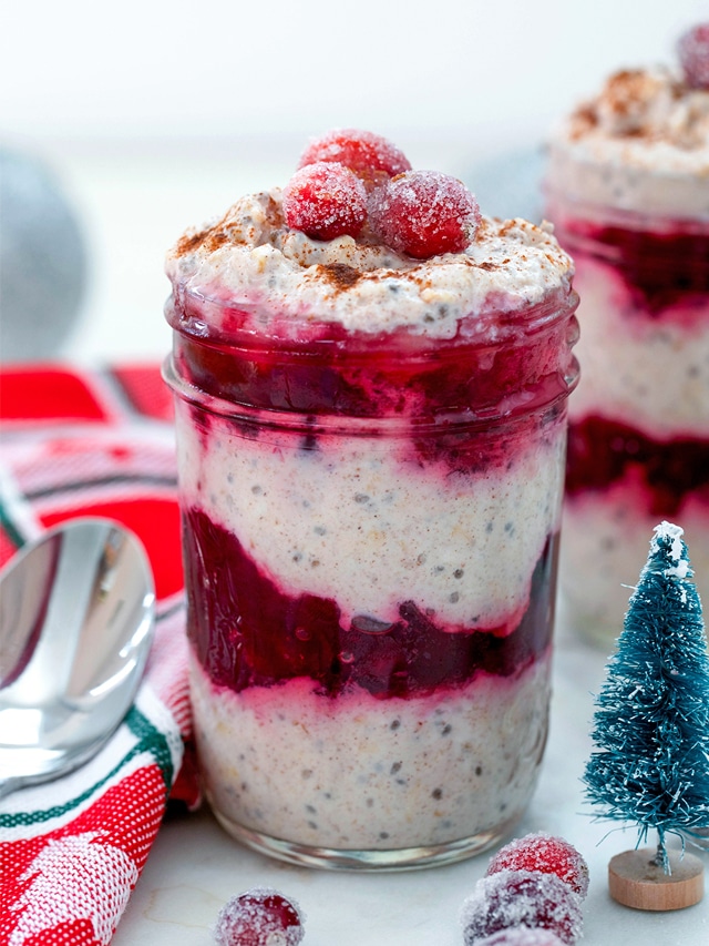 Head-on view of cranberry overnight oats in a small mason jar with spoon and sugared cranberries