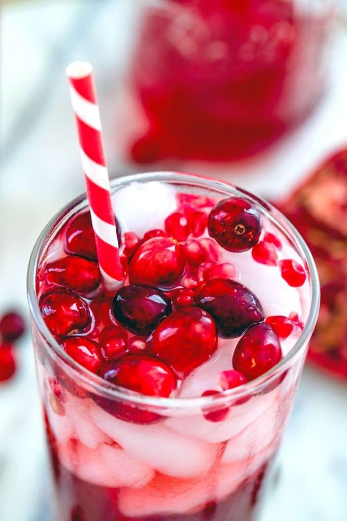 Close-up overhead view of cranberry pomegranate cocktail with cranberry and pomegranate aril garnishes in glass with red and white striped straw