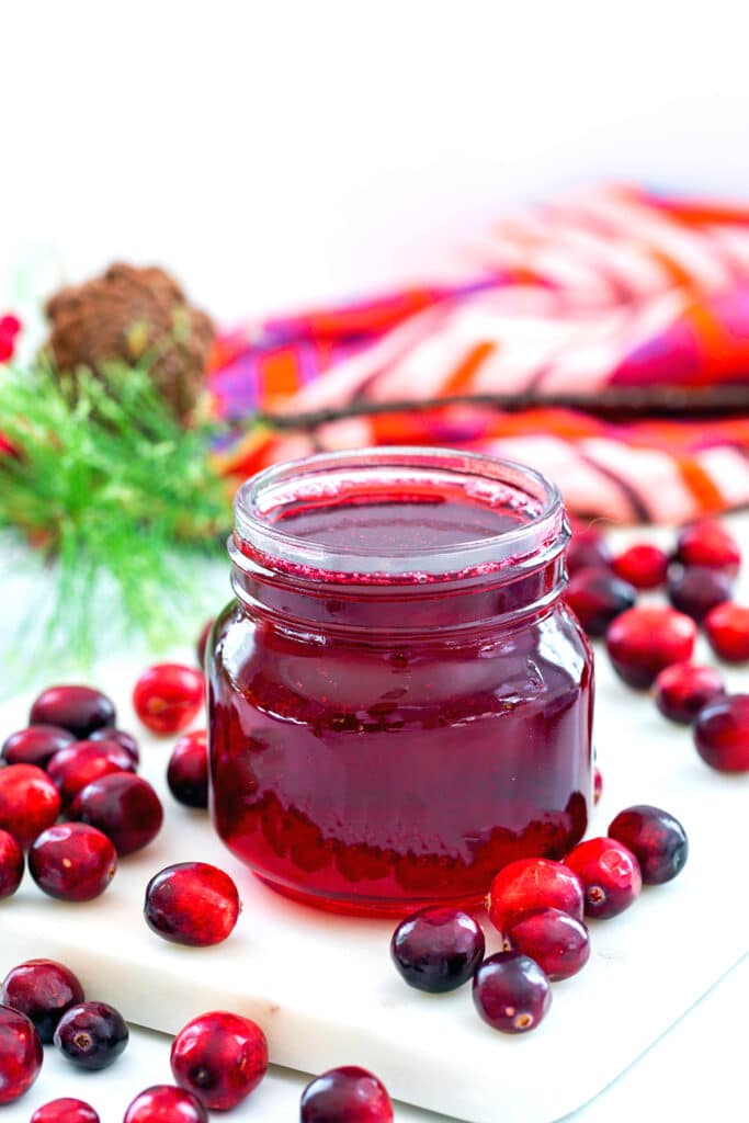 Head-on view of a small jar of cranberry simple syrup with cranberries all around.