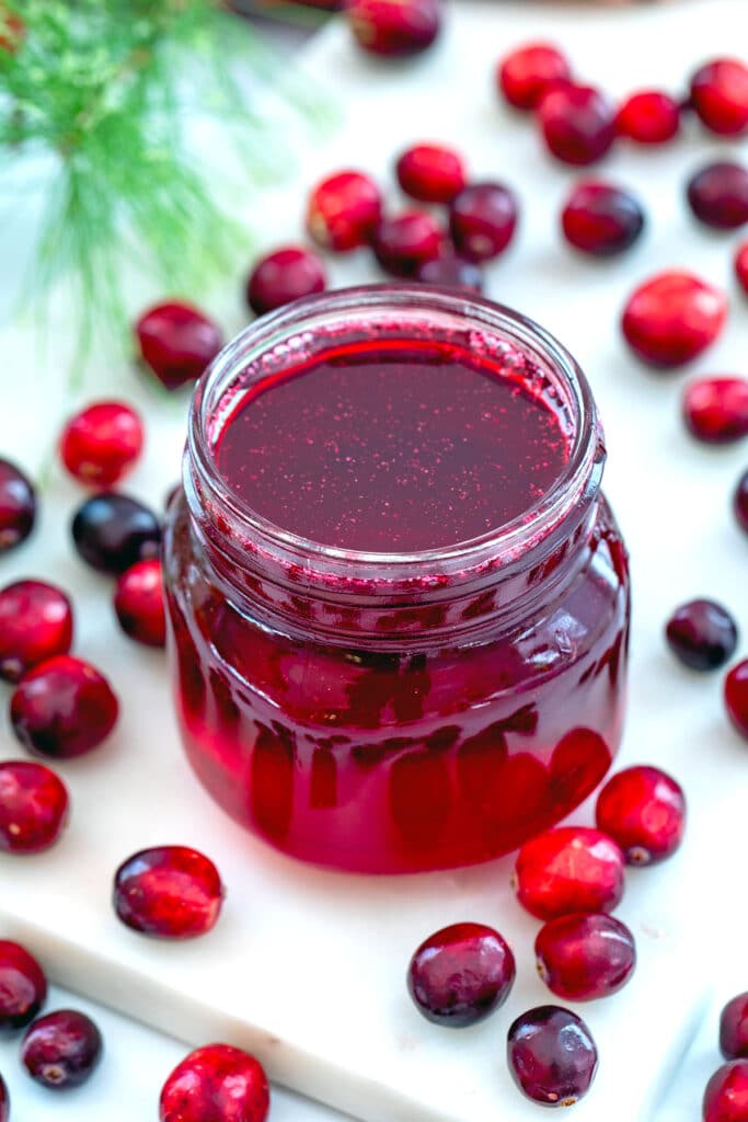 Overhead view of a small jar of cranberry simple syrup with fresh cranberries all around.