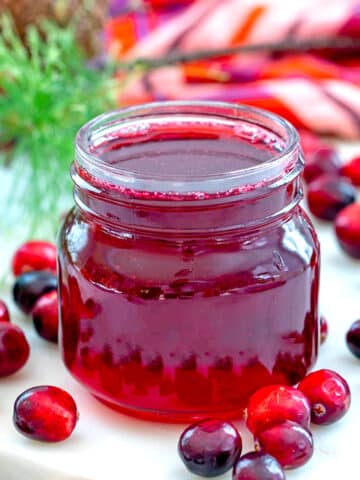 Closeup view of a small jar of cranberry simple syrup with fresh cranberries all around.