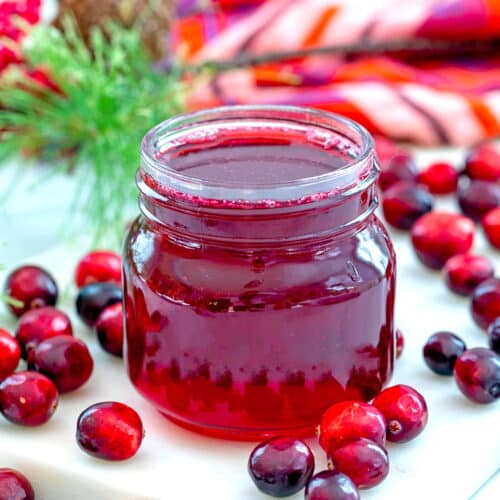 Closeup view of a small jar of cranberry simple syrup with fresh cranberries all around.