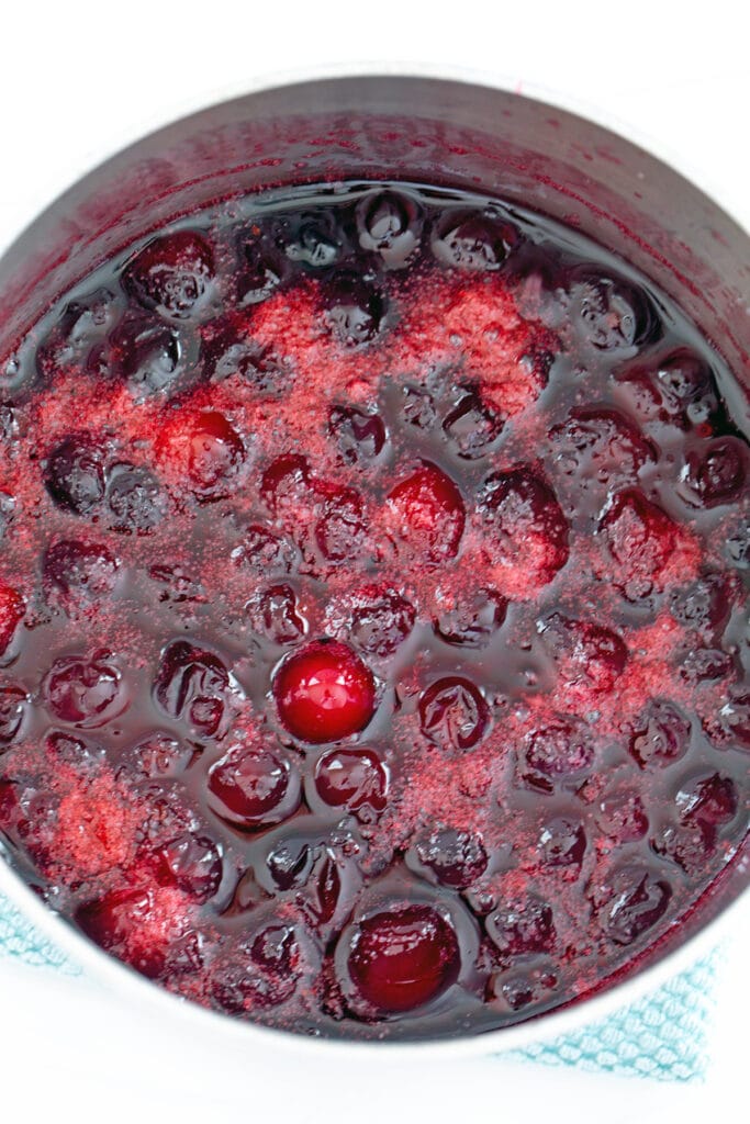 Cranberries simmering in saucepan with sugar and water.