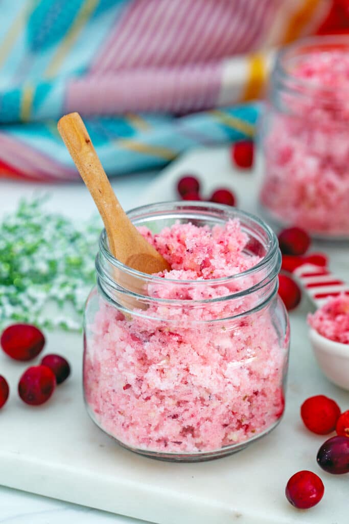 Small jar of pink cranberry sugar with second jar in background and fresh cranberries all around