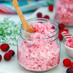 Closeup head-on view of a small jar of pink cranberry sugar with second jar in background and fresh cranberries all around