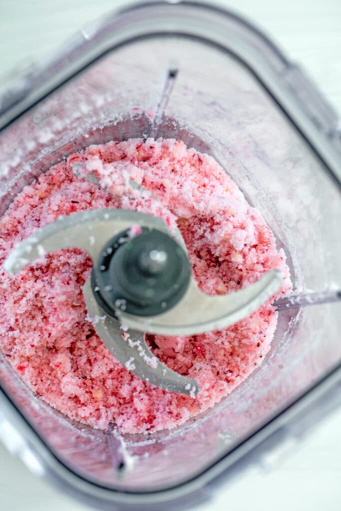 Overhead view of granulated sugar and fresh cranberries blended together into pink sugar in blender
