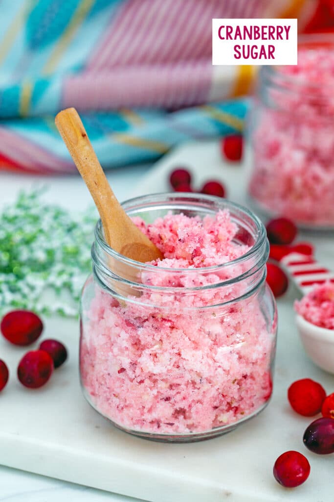 Small jar of pink cranberry sugar with second jar in background, fresh cranberries all around, and recipe title at top