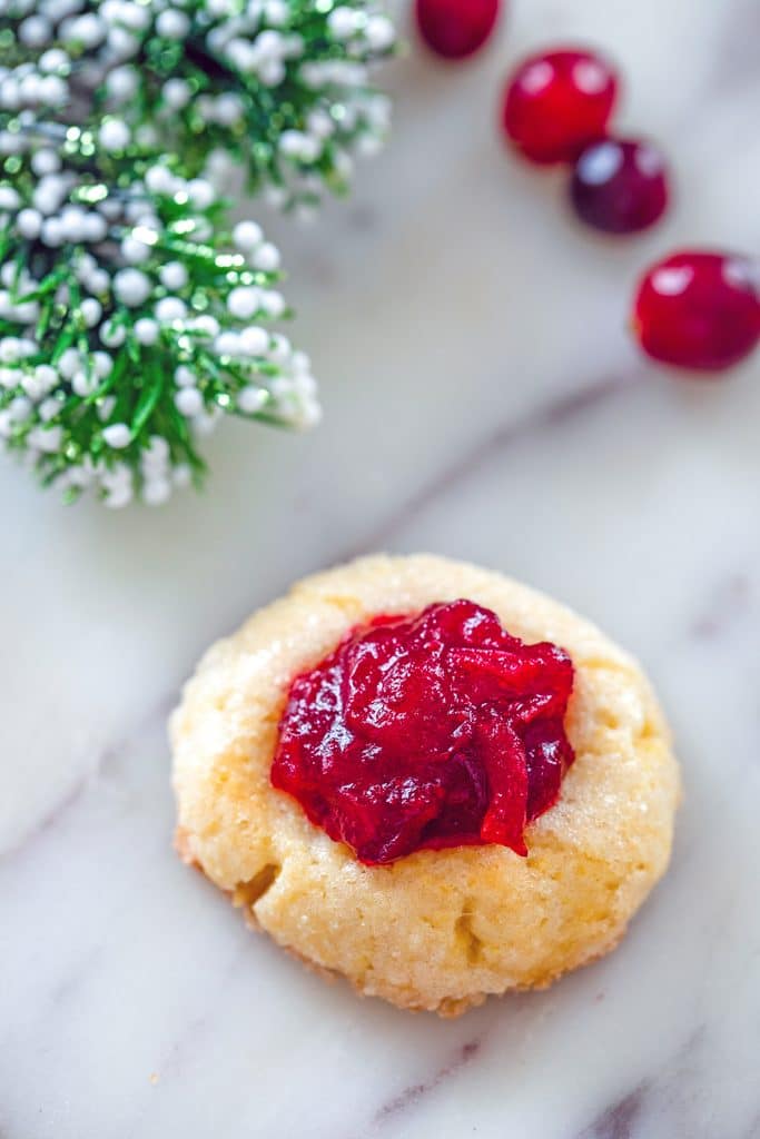 Overhead view of cranberry thumbprint cookie with brand of holly and cranberries in background