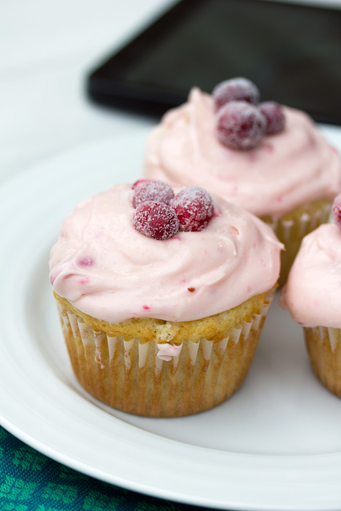Three cranberry champagne cupcakes on a white plate, each with pink cream cheese frosting and sugared cranberries on top