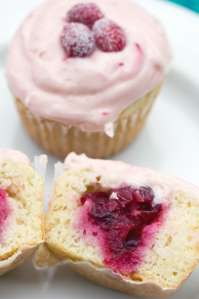 Overhead view of cranberry champagne cupcake with a second cupcake in front and cut in half to show cranberry sauce filling
