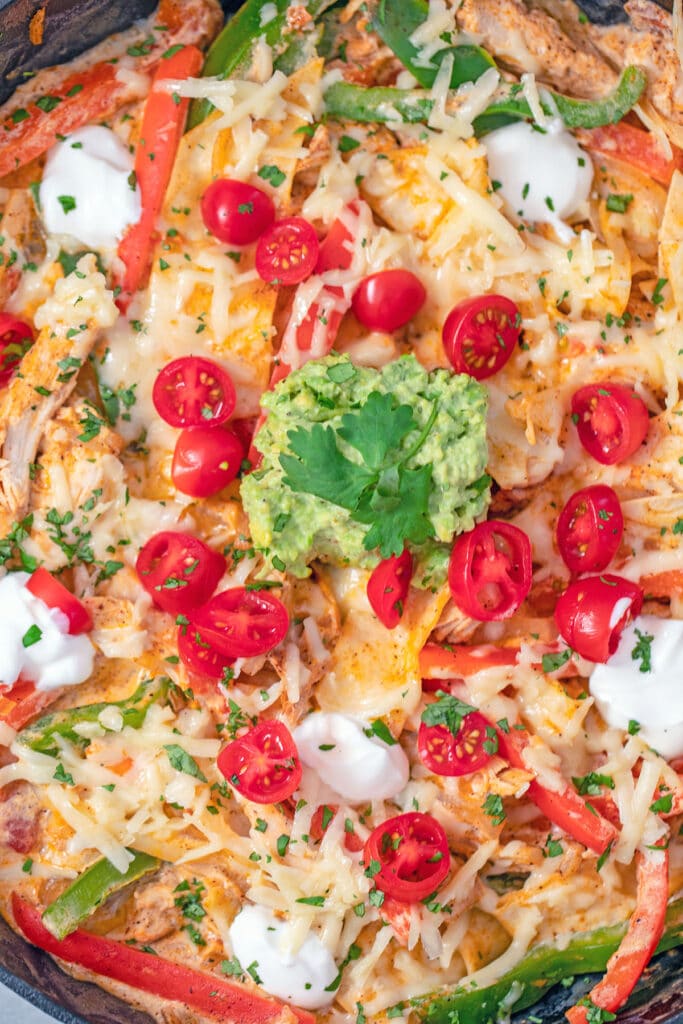 Close-up of creamy fajita skillet with cheese, chicken, peppers, tomatoes, guacamole, and cilantro.