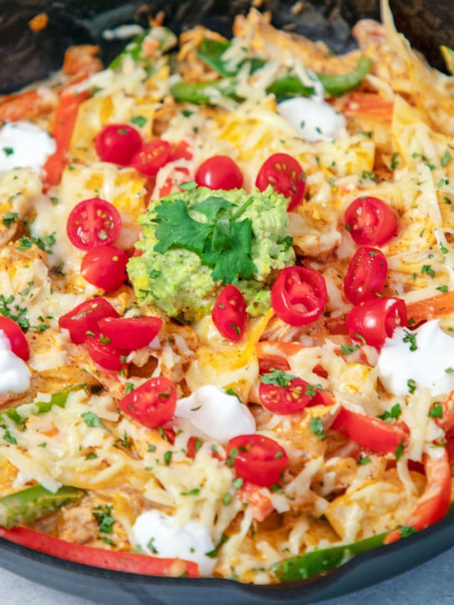 Closeup view of a creamy fajita skillet with tomatoes, guacamole, and cheese.