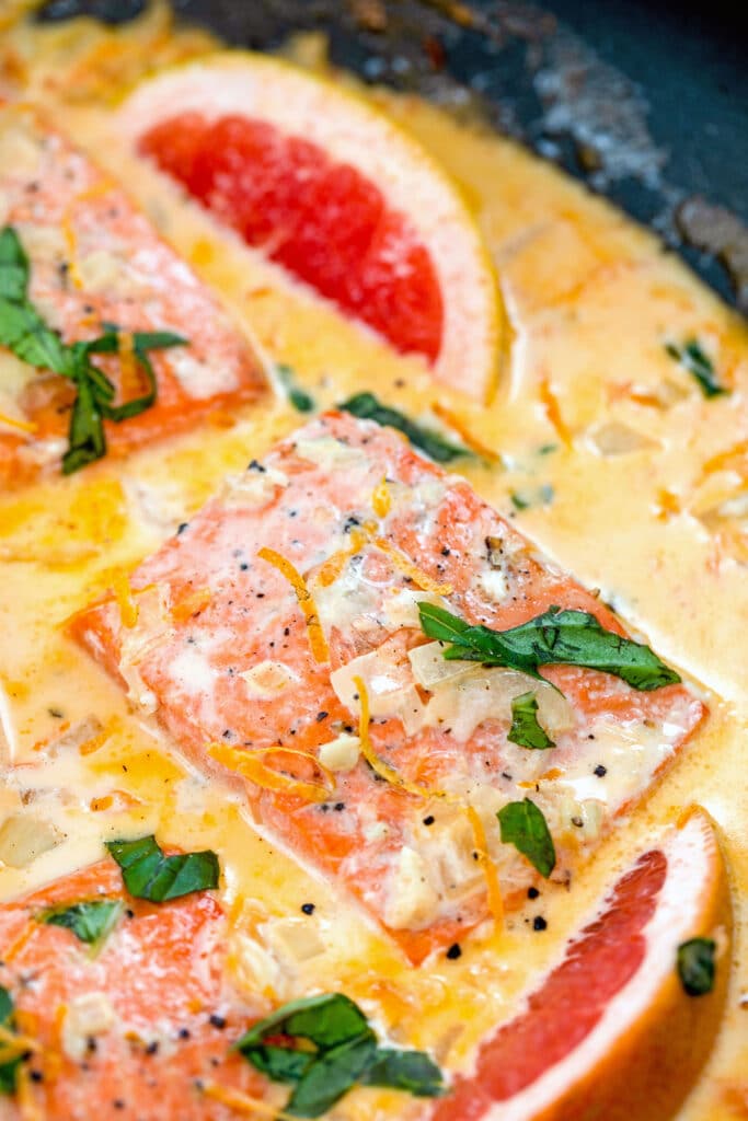 Overhead closeup view of creamy grapefruit salmon in a skillet with basil, grapefruit wedges, and a grapefruit cream sauce.