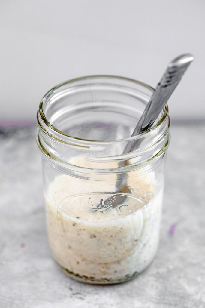 Head-on view of creamy lemon dressing in a mason jar with a spoon