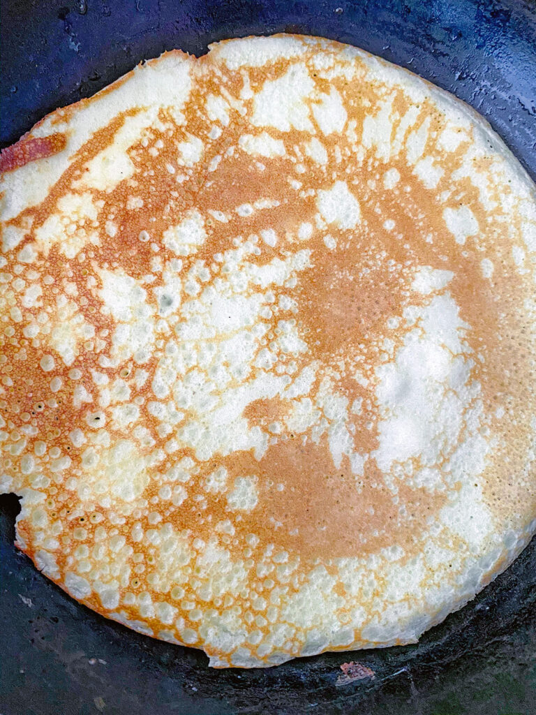 Overhead view of crepe just flipped and cooking in pan