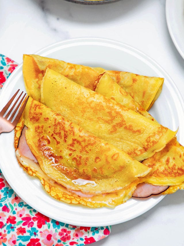 Crepes with pancake mix and stuffed with ham and cheese with maple syrup on white plate with fork.