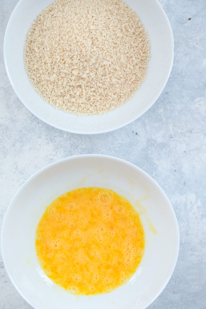 Overhead view of two bowls, one filled with panko and one filled with lightly beaten eggs