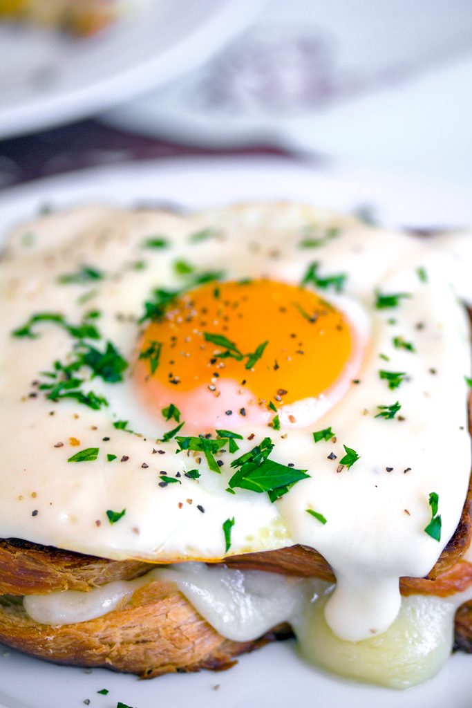 Overhead close-up view of a croque madame with perfectly cooked egg on top, mornay sauce, and chopped parsley with cheese oozing out