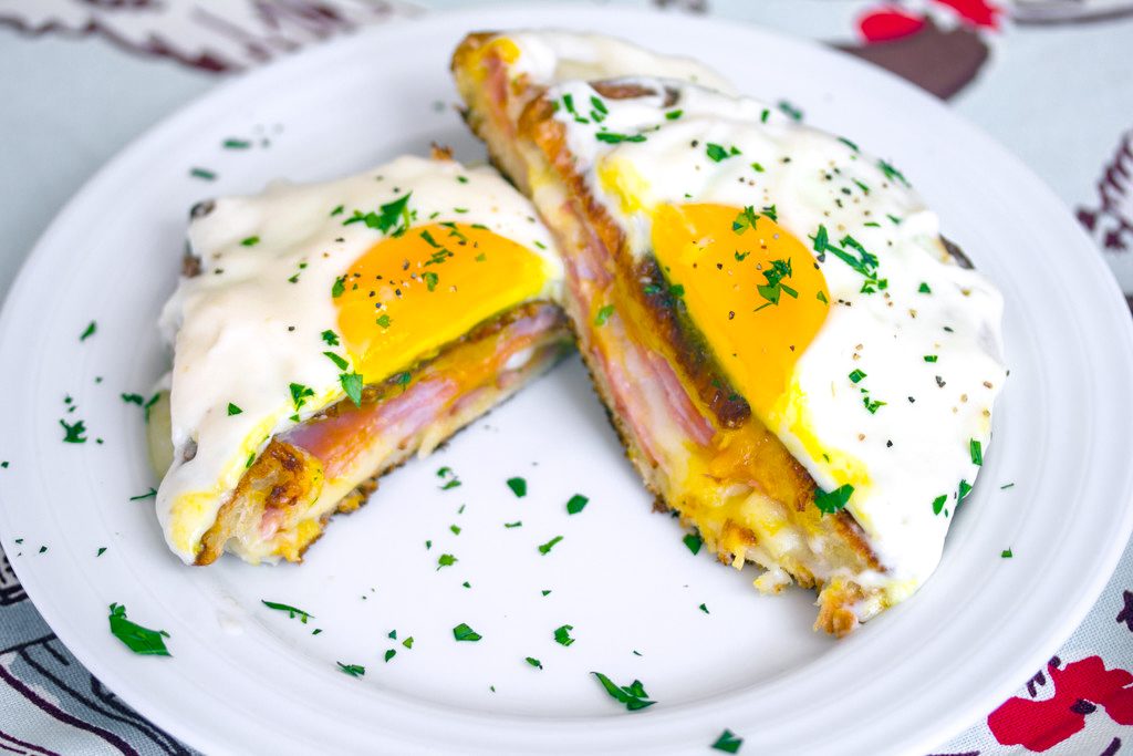 Landscape bird's eye view of a croque madame cut in half on a white plate with parsley sprinkled all around