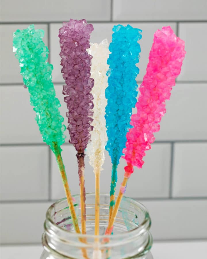 Mason jar filled with 5 different colors of rock candy on sticks.