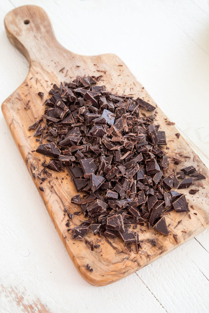 Chopped dark chocolate on wooden board.