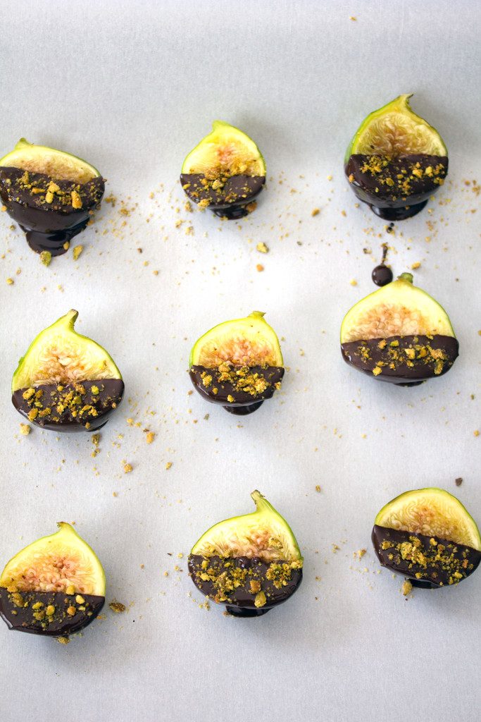 Three rows of three figs dipped in dark chocolate and topped with pistachios drying on parchment paper