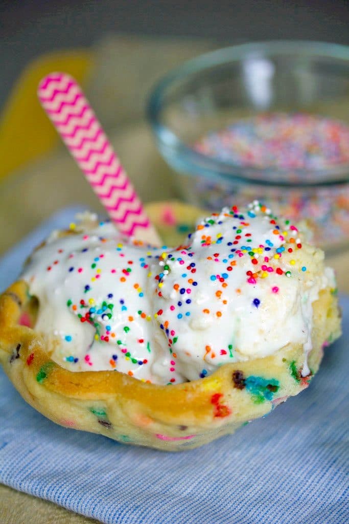 Head-on view of edible cookie bowl filled with ice cream, marshmallow sauce, and sprinkles with pink chevron spoon and sprinkles in the background