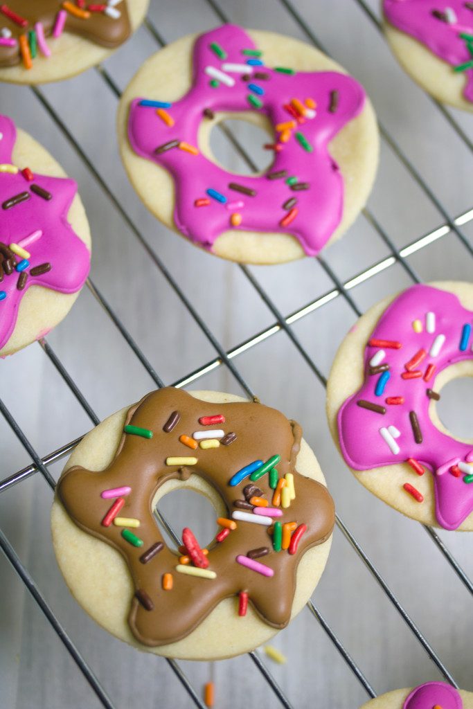 Overhead view of multiple doughnut sugar cookies with pink and brown frosting and sprinkles on baking rack