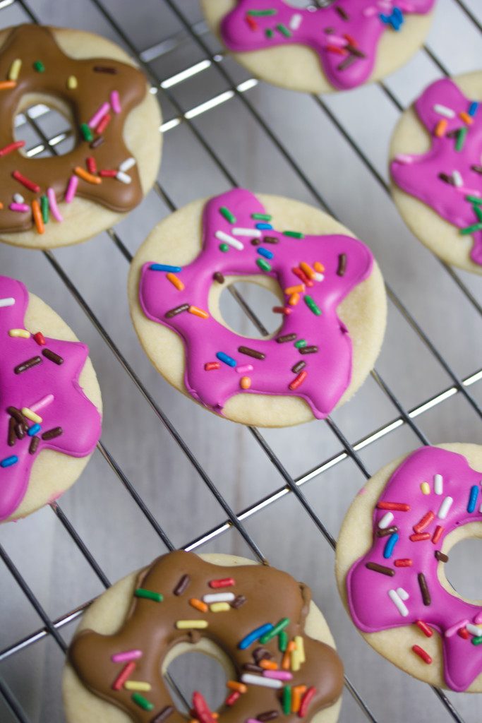 Close-up of multiple doughnut sugar cookies with pink and brown icing on a baking rack