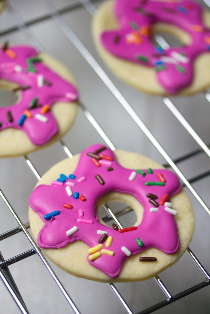 Close-up of a pink frosted doughnut sugar cookie with sprinkles on a baking rack