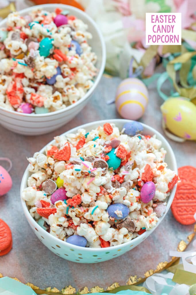View of a bowl of Easter candy popcorn with M&Ms, sprinkles, and Easter Oreo cookies with second bowl and Easter eggs in background and recipe title at top