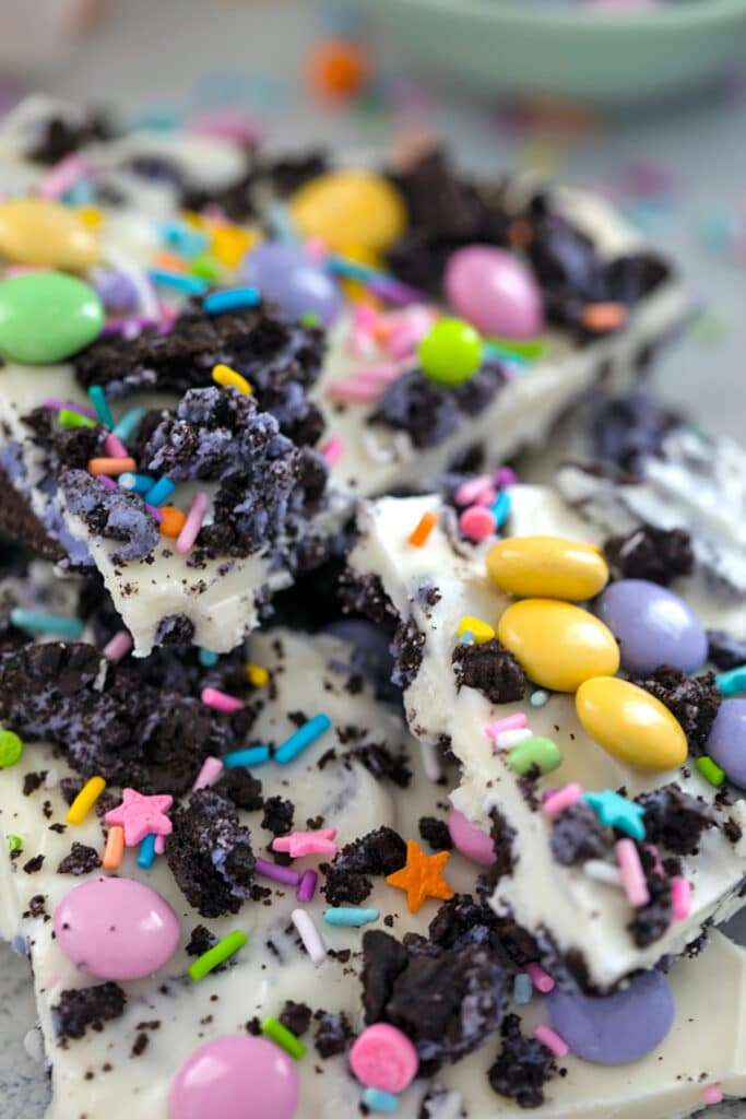 Closeup view of multiple pieces of white chocolate Easter Oreo bark with spring M&Ms, crushed Peeps Oreo cookies, and pastel sprinkles.