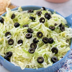 Close-up view of easy taco dip in pie plate topped with shredded lettuce and sliced olives