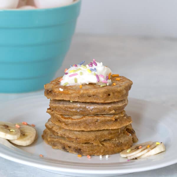 Head-on view of a stack of egg, apple, and banana pancakes for dogs with whipped cream and sprinkles and sliced bananas all around