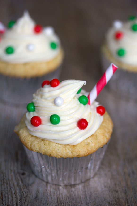 Overhead view of an eggnog cupcake with eggnog frosting, red and green decorations, and a red and white straw with more cupcakes in background
