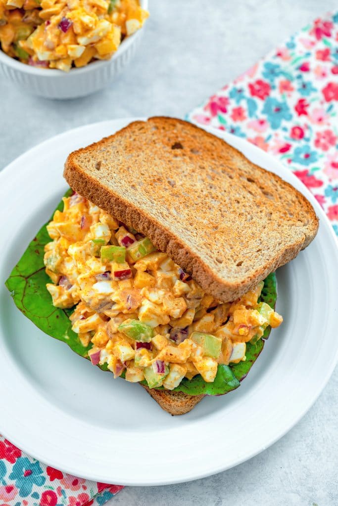 Bird's eye view of egg salad with lots of crunch on a sandwich with Swiss chard with bowl of more egg salad in the background