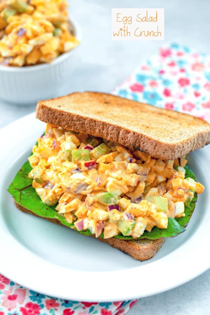 Head-on view of a sandwich with egg salad with lots of crunch with Swiss chard and with a bowl of more crunchy egg salad in the background with recipe title at top