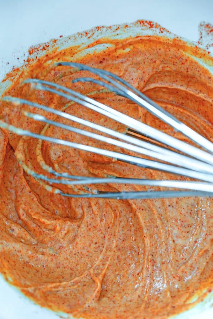 Overhead view of mayo dressing with cayenne and paprika in bowl with whisk