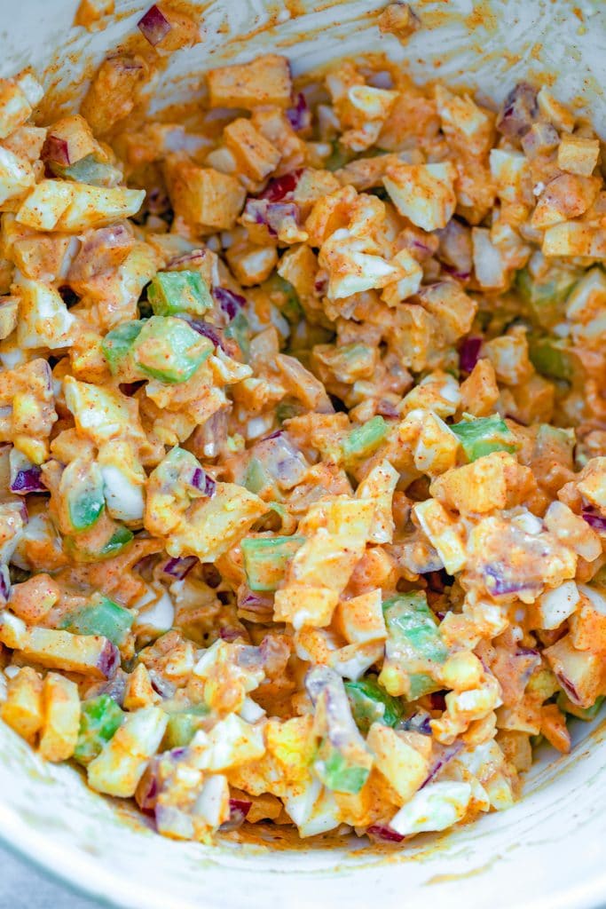 Overhead view of egg salad with lots of crunch in a mixing bowl with mayo dressing on it