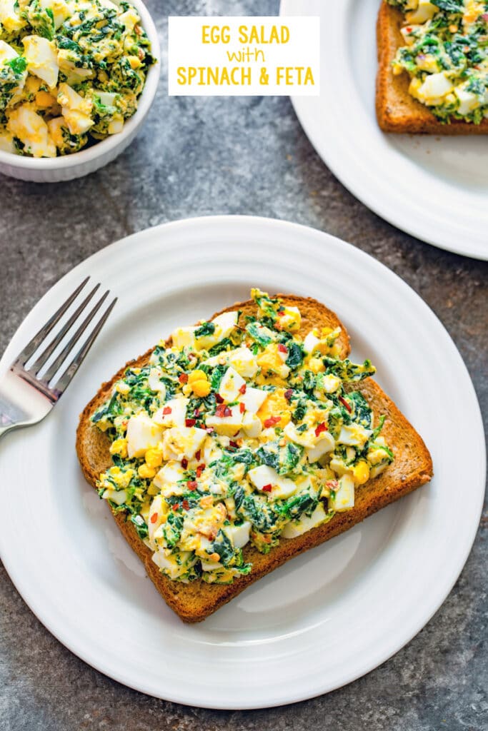 Overhead view of a slice of whole wheat toast with egg salad with spinach and feta on it with more egg salad in background and recipe title at top of image