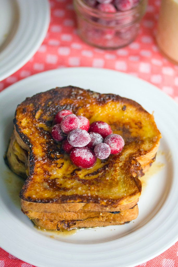 Overhead closeup view of eggnog french toast topped with sugared cranberries on white plate