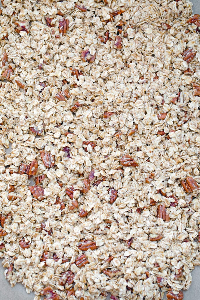 Granola mixture spread out on baking sheet ready to go in oven