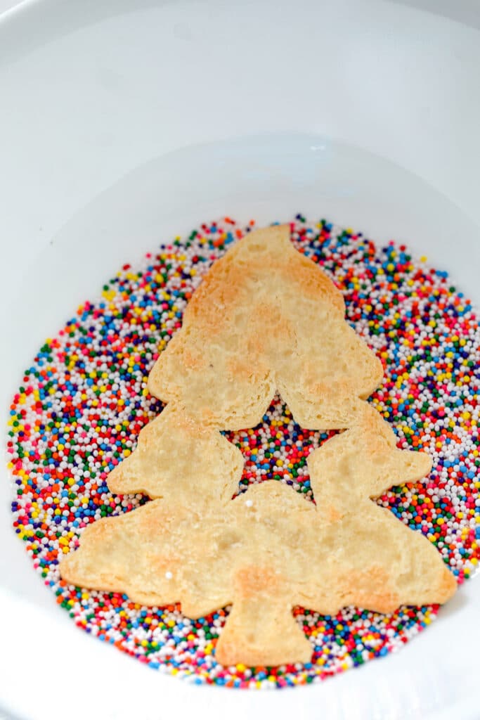 Christmas tree cookie upside down in bowl of sprinkles