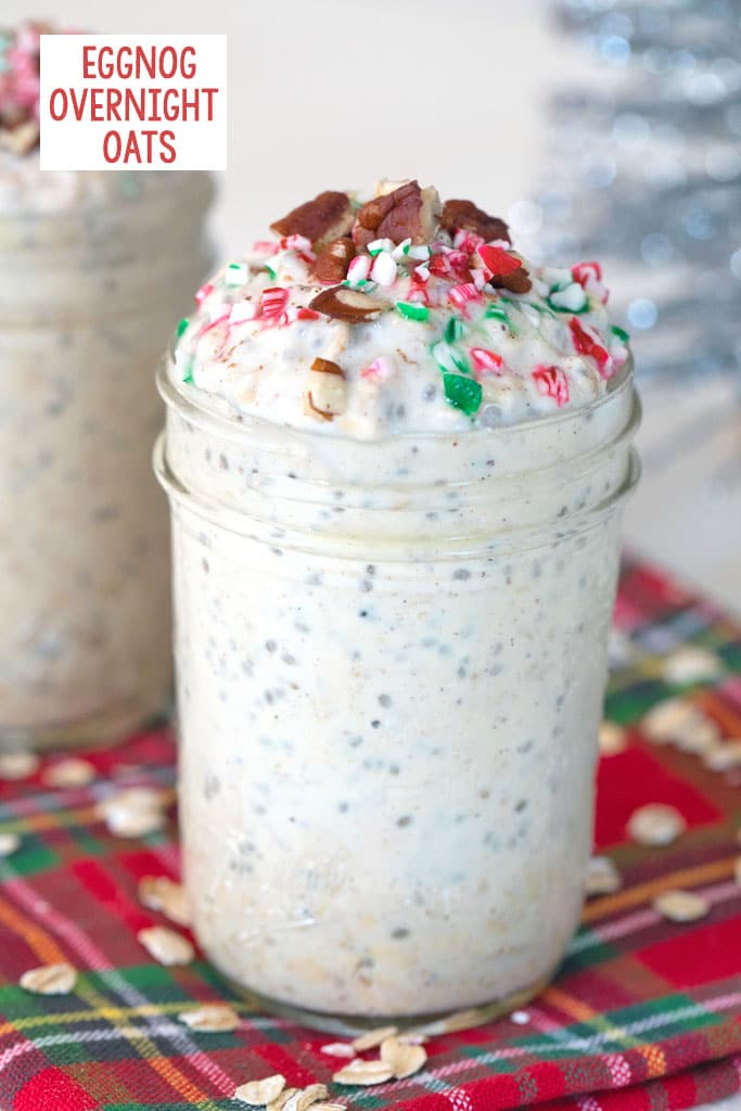 Head-on view of a mason jar filled with eggnog overnight oats topped with crushed candy canes and pecans with second jar and silver tinsel in the background and recipe title at top