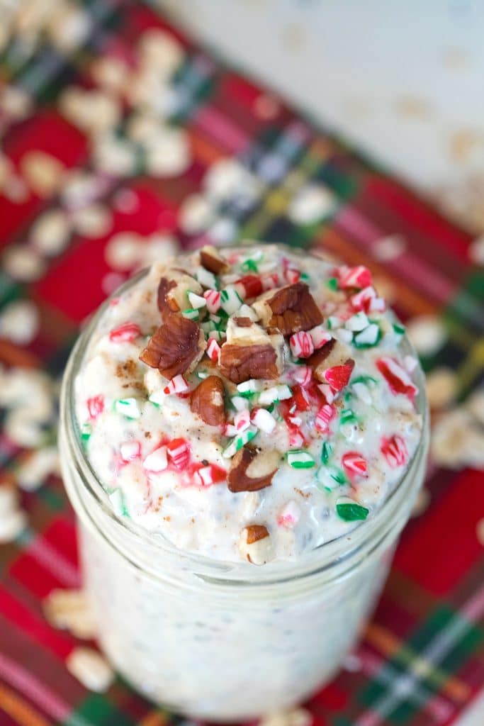 Overhead view of a jar of eggnog overnight oats topped with crushed red, white, and green candy canes and pecans with oats scattered all around