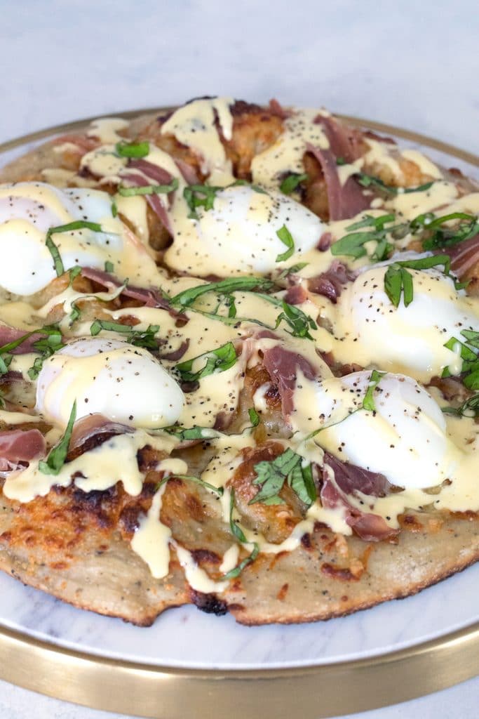 Head-on view of eggs benedict pizza with sous vide eggs, prosciutto, and hollandaise sauce drizzled over the top