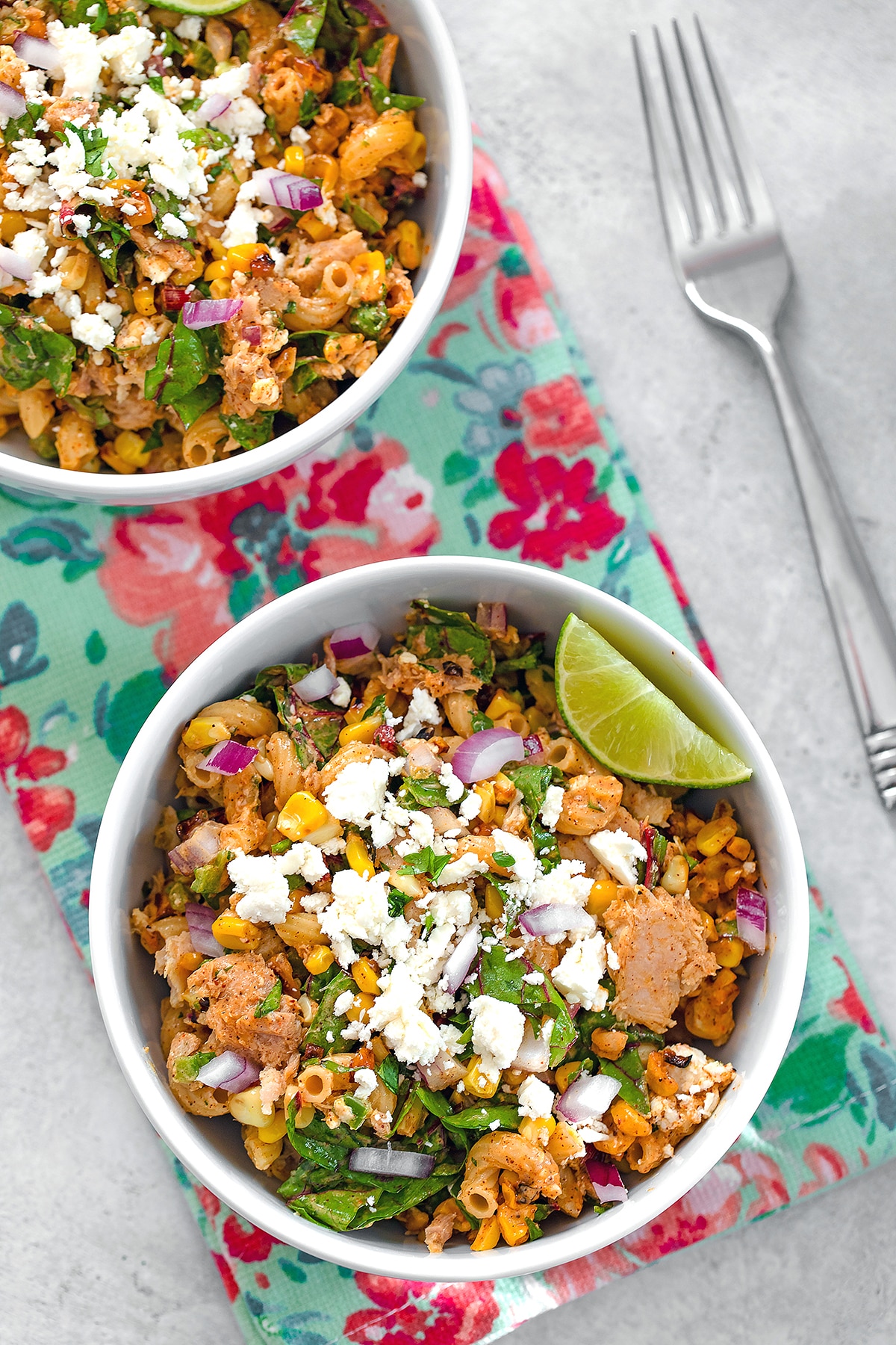Bird's eye view of two bowls of elote tuna salad on a flowered towel with a fork in the background.