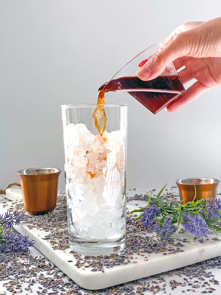 Espresso being poured into ice-filled glass with lavender flowers all around