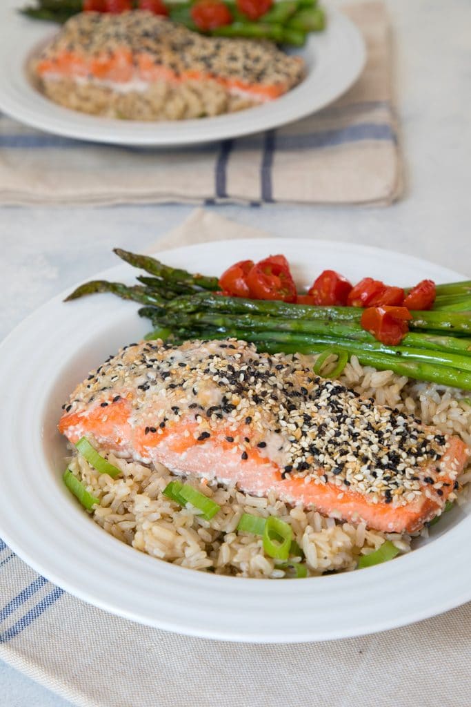 View from a distance of everything bagel salmon served over a bed of brown rice with asparagus and grape tomatoes.