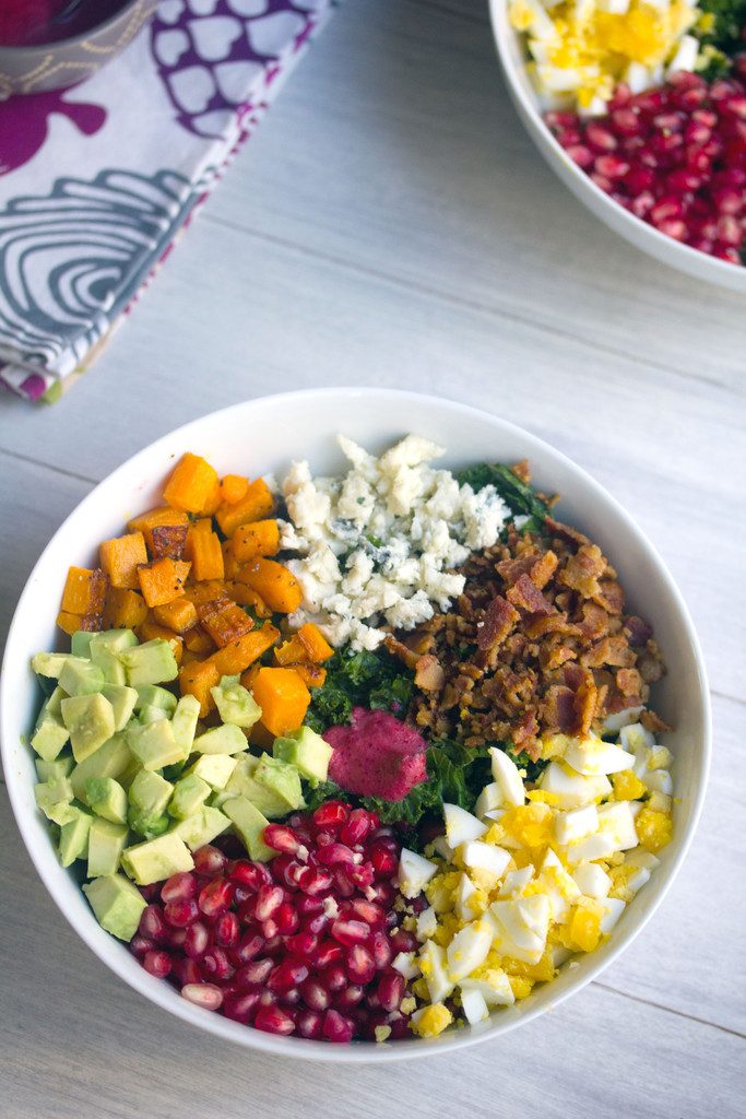 Overhead view of fall kale salad with kale, pomegranate, avocado, butternut squash, gorgonzola, bacon, and hardboiled eggs